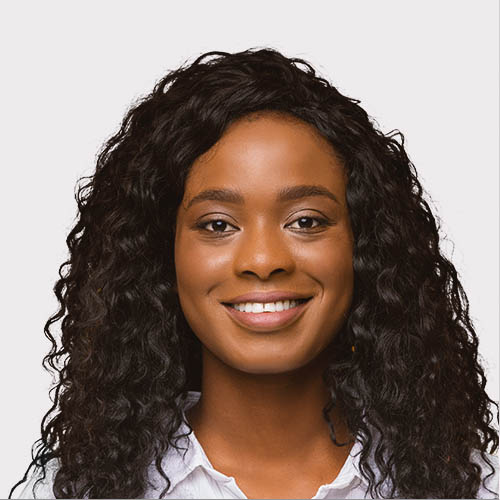 A smiling woman with curly hair is wearing a white shirt, conveying a friendly and approachable demeanor. The background is plain, emphasizing her expression.