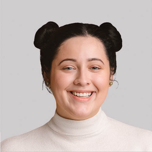 A smiling woman with two buns in her hair is wearing a white turtleneck. The background is plain and light-colored.